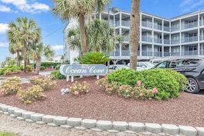 A multi-story hotel with a sign reading "Ocean Cove" and a parking area with cars.
