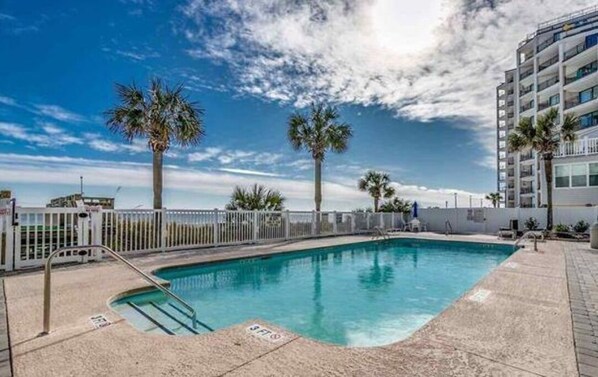 A rectangular pool with a white fence, palm trees, and a clear blue sky.