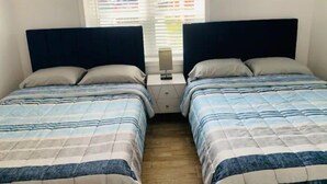Habitación doble con dos camas, cada una con cubrecama azul y blanco a rayas, cabecero oscuro y mesita de noche con lámpara.