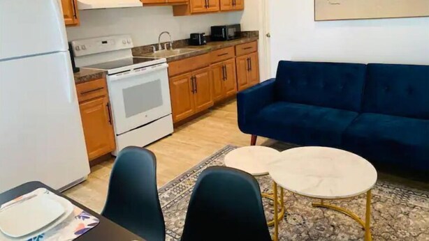 Un espacio habitable compacto con kitchenette, un sofá azul, una mesita redonda y vistas a la playa.