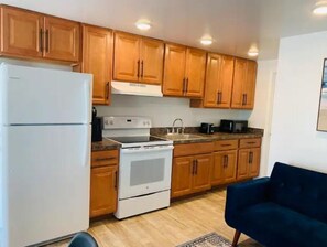 Compact kitchen with refrigerator, stove, and microwave, adjacent to a cozy living space with a sofa.