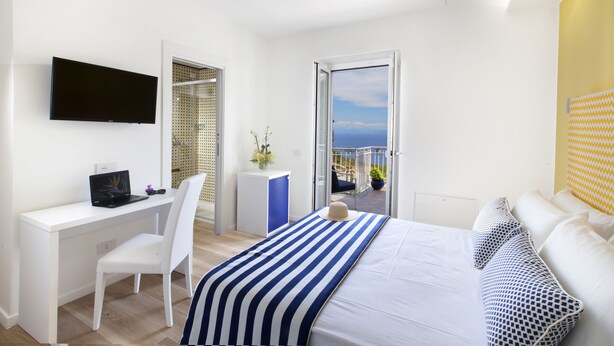 A modern hotel room with a bed, a desk with a computer, a chair, and a TV. - Relais Loggia Li Galli (Massa Lubrense)