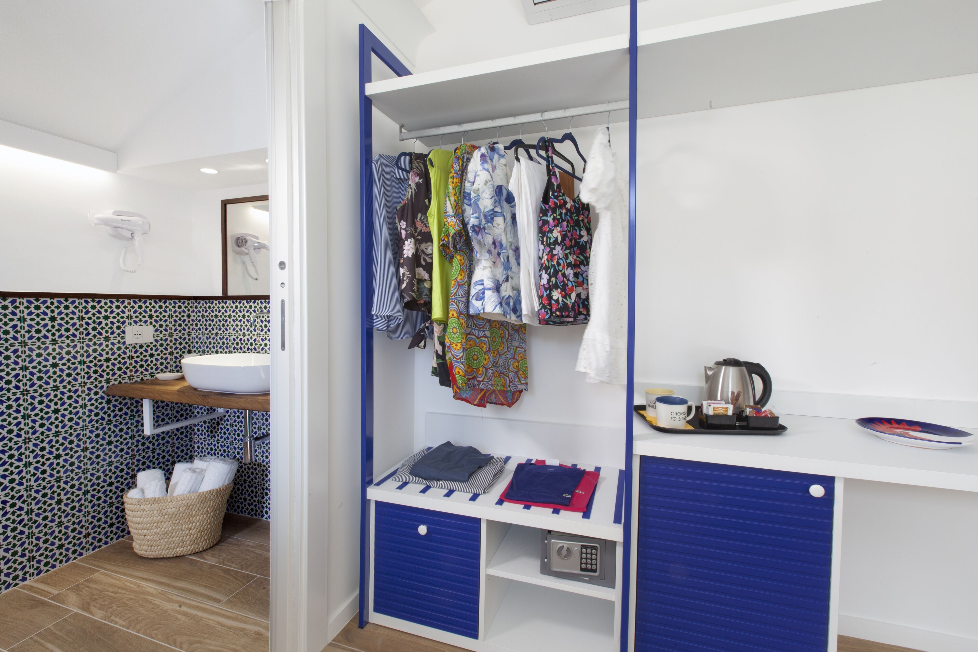 Un baño con un lavamanos blanco, un salpicadero de azulejos azul y blanco, una cesta blanca para toallas y un armario azul.