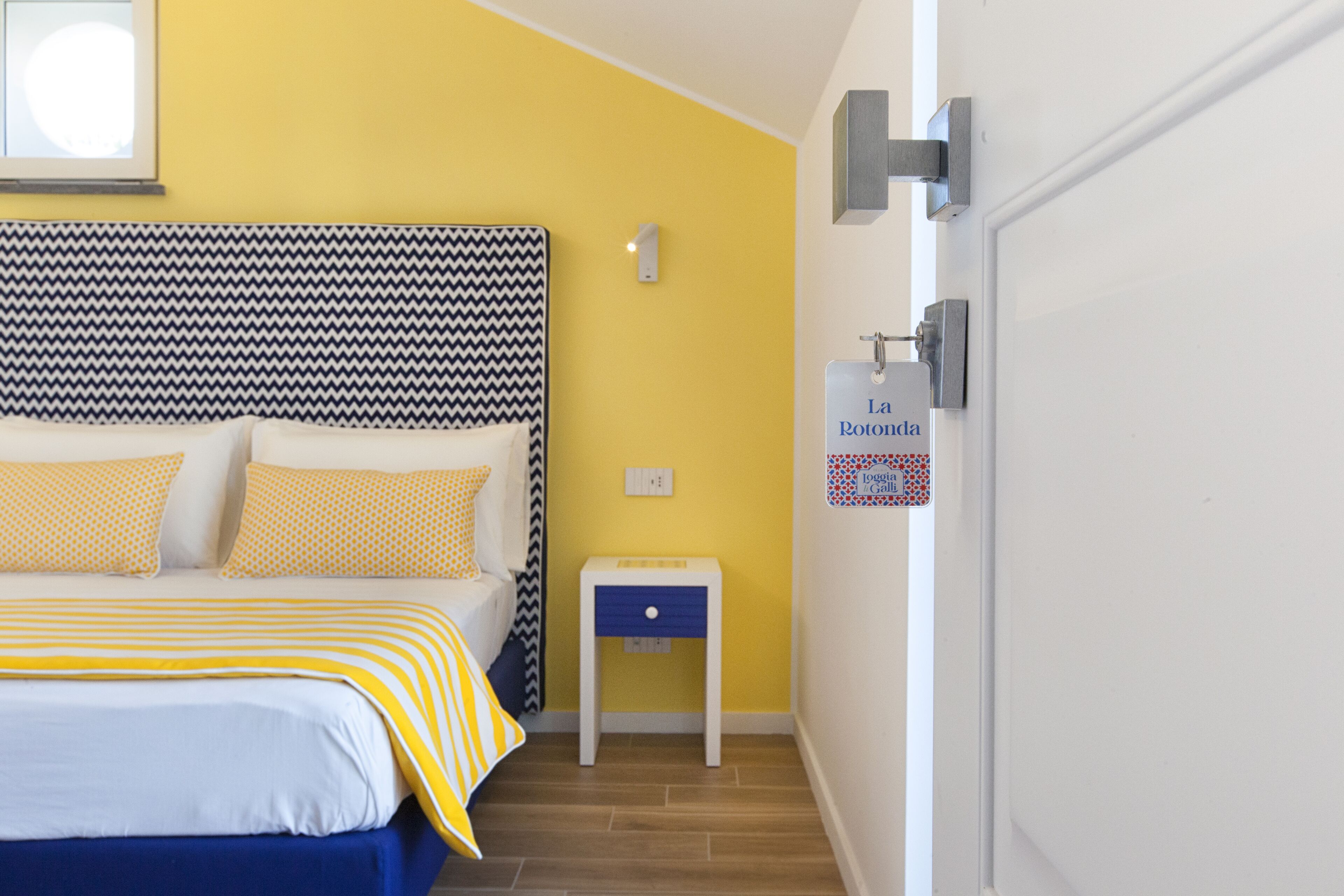 Ein Hotelzimmer mit Bett, einem kleinen Nachttisch, einer Wandleuchte und einer Tür mit einem Schild.