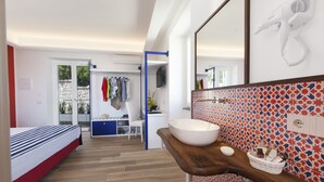 A modern bedroom with a bed, a desk, and a bathroom with a large mirror and a sink. - Relais Loggia Li Galli (Massa Lubrense)