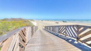Een houten looppad dat naar een strand leidt, met een heldere lucht.