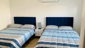 Camera da letto con due letti, ciascuno con una testata blu, un comodino con una lampada e un condizionatore d'aria a parete.
