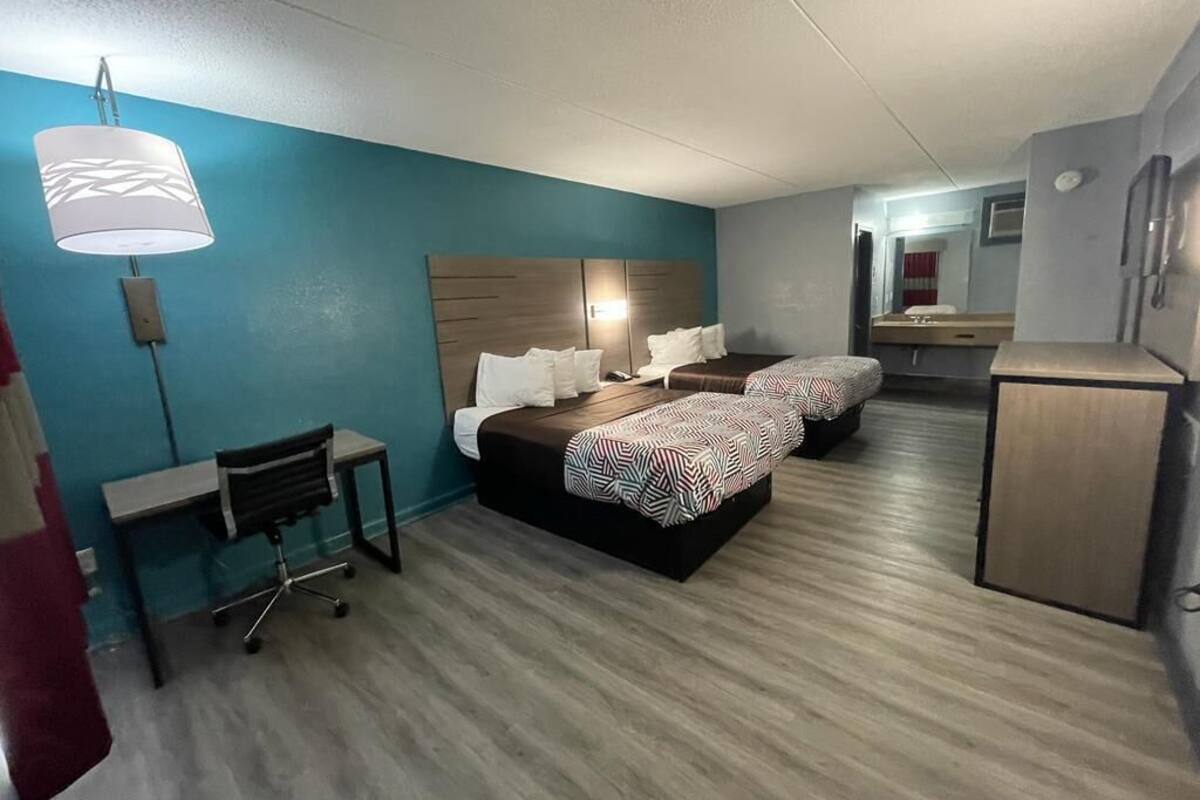 Una habitación de hotel con cama, escritorio, silla y una pequeña kitchenette.