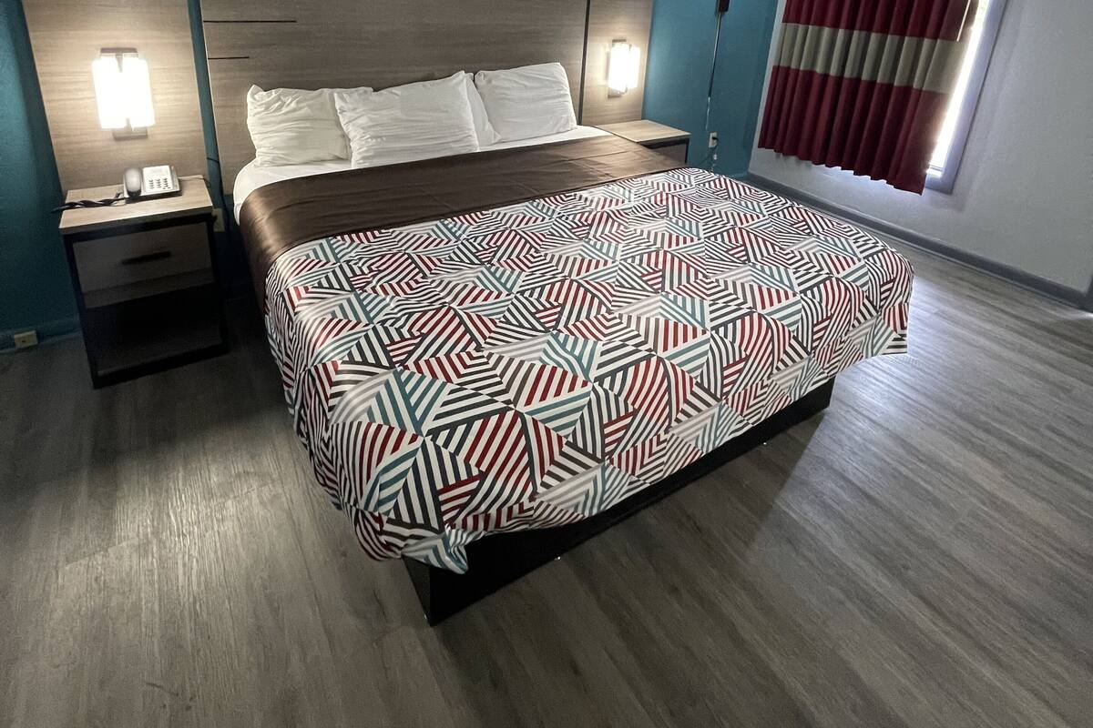 Habitación de hotel con cama, dos mesitas de noche, una lámpara de pared y un ventanal con cortinas.