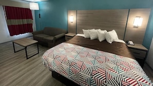 A hotel room with a bed, a sofa, a small table, and a nightstand with a lamp. - Jackson motel  (Murfreesboro)