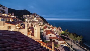 Eine Küstenstadt im Abenddämmerung mit terrassenförmig angelegten Gebäuden, einem Strand und Blick aufs Meer.