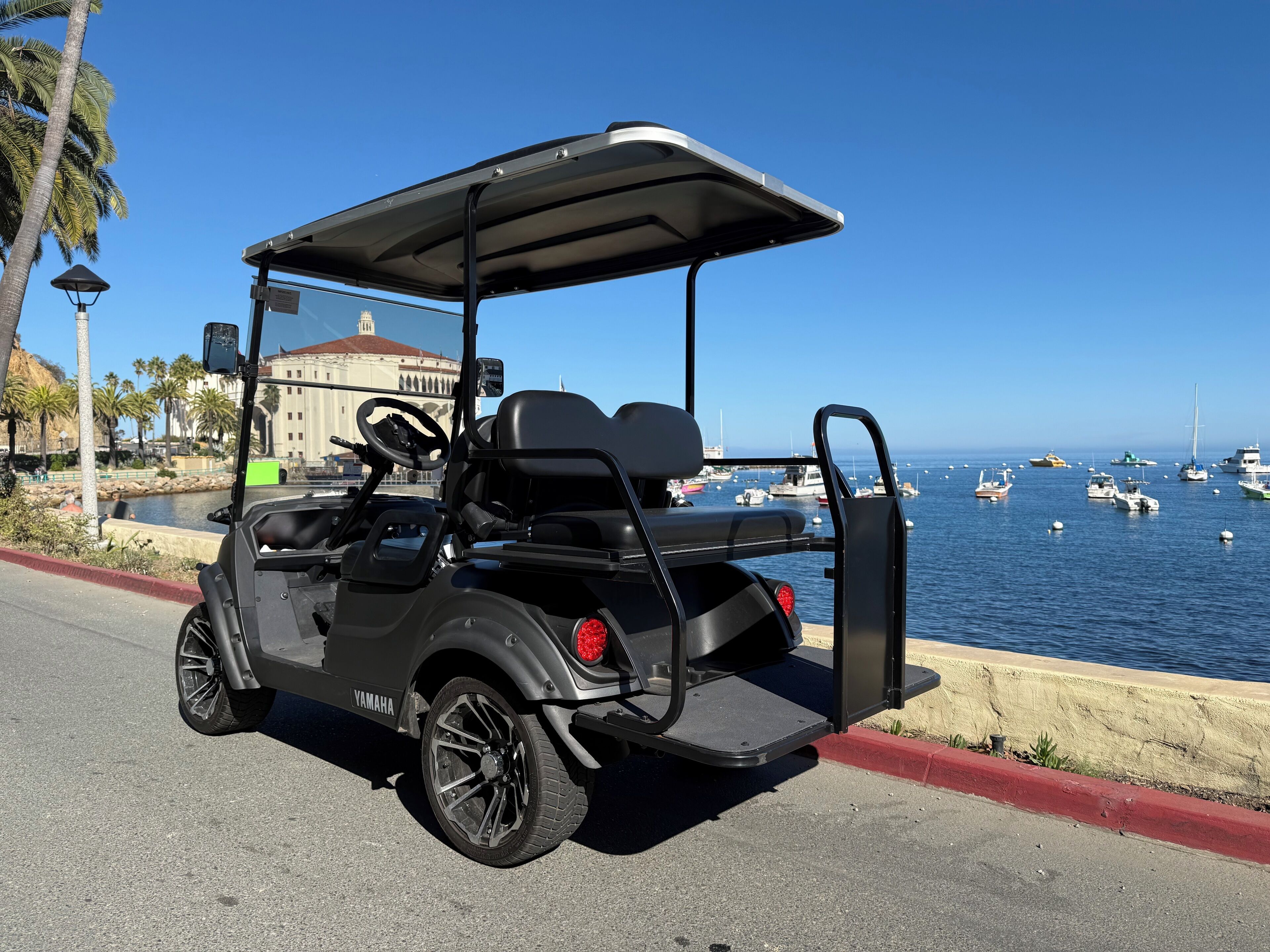 Ein schwarzer Golfwagen steht am Ufer, im Hintergrund sind Boote zu sehen.