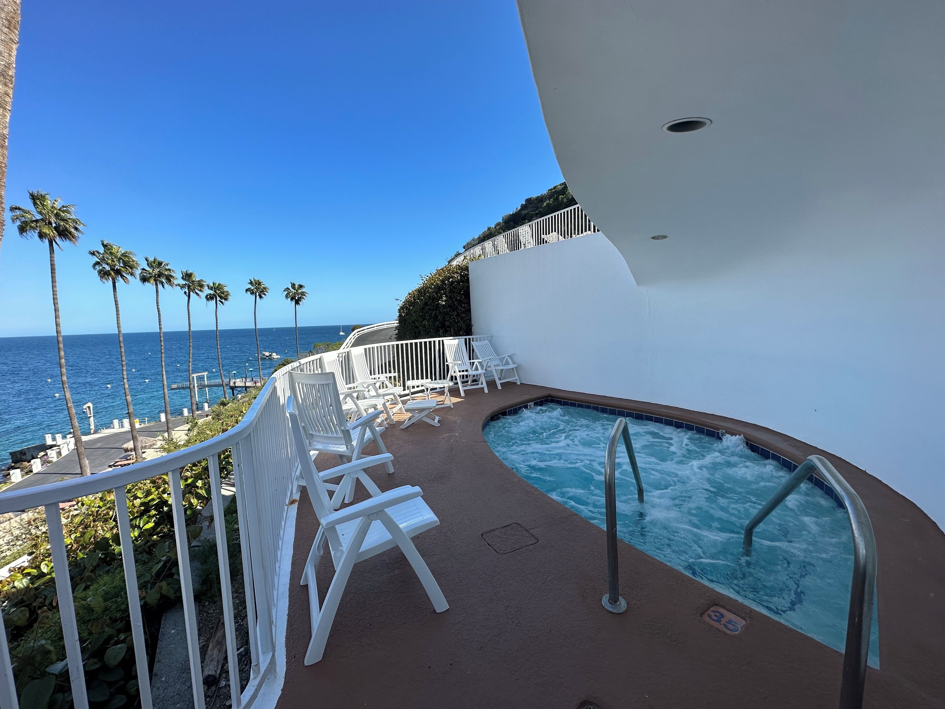 Zona de piscina con sillones blancos y vista al océano.