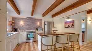 A kitchen with wooden beams, a brick backsplash, stainless steel appliances, and a bar area with stools. - Private Hot Tub & Deck: North Conway Retreat (North Conway)