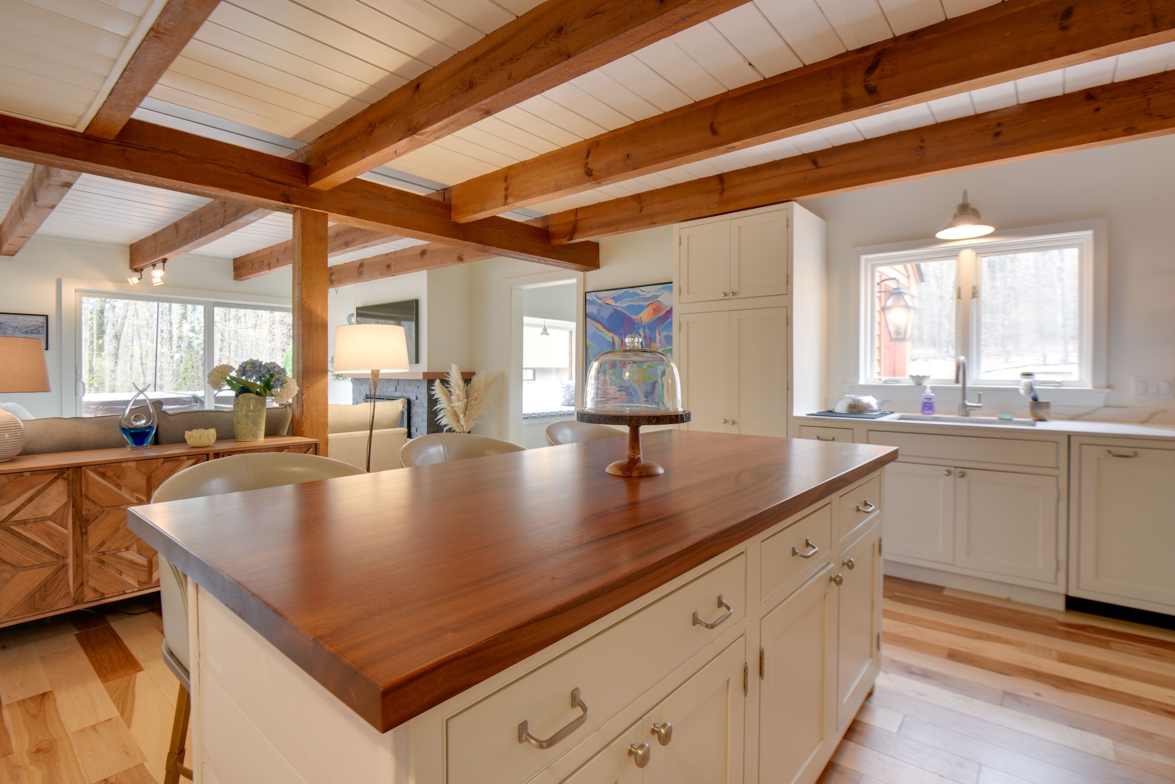 Una cocina con vigas de madera, armarios blancos y encimera de madera.