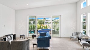 Un salón moderno con un sofá azul, una televisión y vistas a una piscina y vegetación.