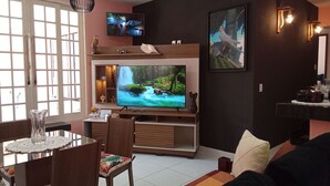A living room with a TV, a dining area, and a black wall with a framed picture.