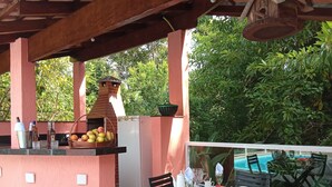 An outdoor dining area with a grill, table, chairs, and a view of a swimming pool.