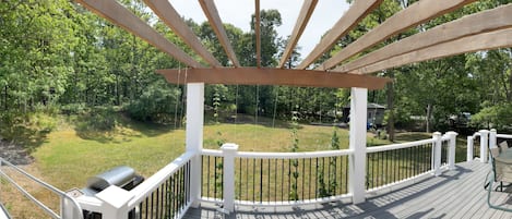 A wooden deck with a grill and outdoor furniture, surrounded by a white railing and a view of a wooded area.