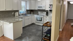 Uma cozinha moderna com armários brancos, bancada de granito, micro-ondas embutido e espaço para vinhos.
