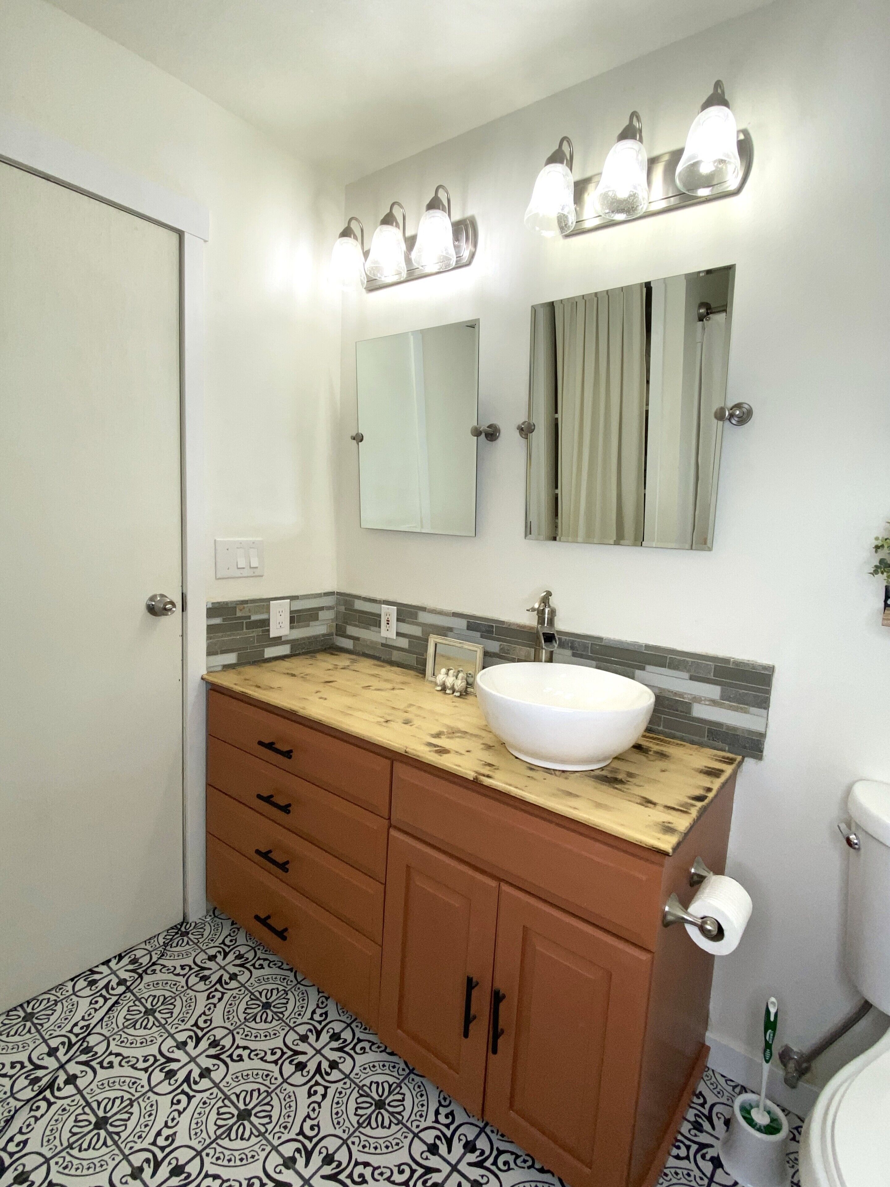 Un baño con lavamanos blanco, tocador de madera y un espejo grande sobre el lavamanos.