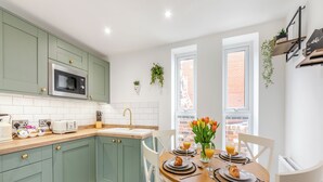 A modern kitchen with teal cabinets, a wooden countertop, and a dining area with a round table set for two. - 2 bedroom accommodation in Redcar (Redcar)