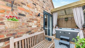 A wooden bench, a hot tub, and a brick wall with a hanging flower basket. - 2 bedroom accommodation in Redcar (Redcar)