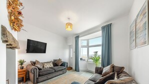 A modern living room with a grey sofa, a blue armchair, and a large window with curtains. - 2 bedroom accommodation in Redcar (Redcar)