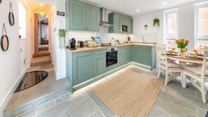 A modern kitchen with teal cabinets, a central island, and a dining area with a table set for two. - 2 bedroom accommodation in Redcar (Redcar)