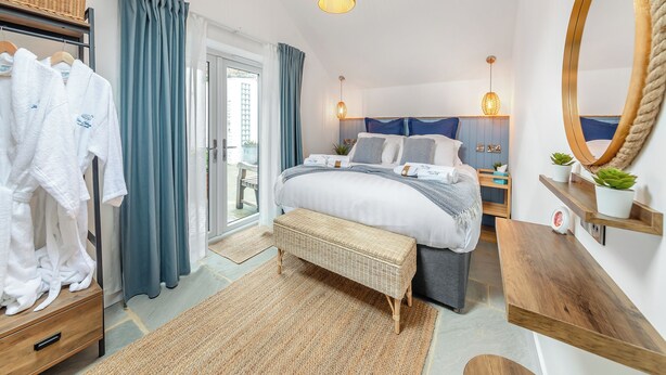 A bedroom with a bed, bedside tables, a bench, a wardrobe, and a large mirror. - 2 bedroom accommodation in Redcar (Redcar)