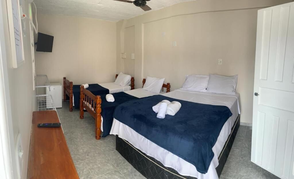 Quarto de hotel com três camas, uma escrivaninha, uma cadeira, uma televisão e uma porta.