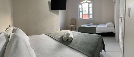 A hotel room with two beds, a flat-screen TV mounted on the wall, a window with a view, and a chair.