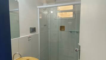 Un baño con ducha de vidrio, un lavamanos amarillo y un inodoro.