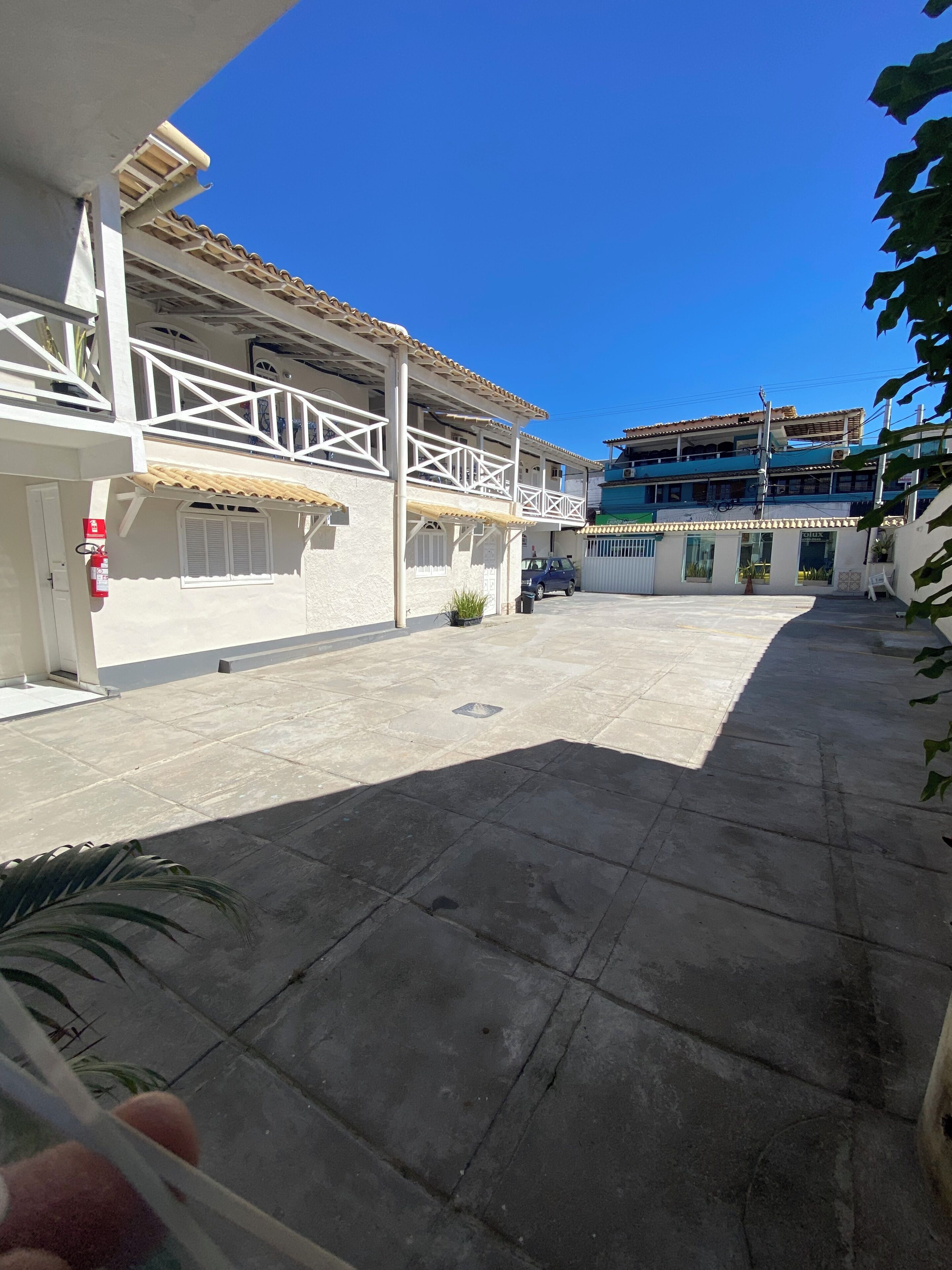 A courtyard with a tiled floor, a white building with a balcony, and a blue building in the background.