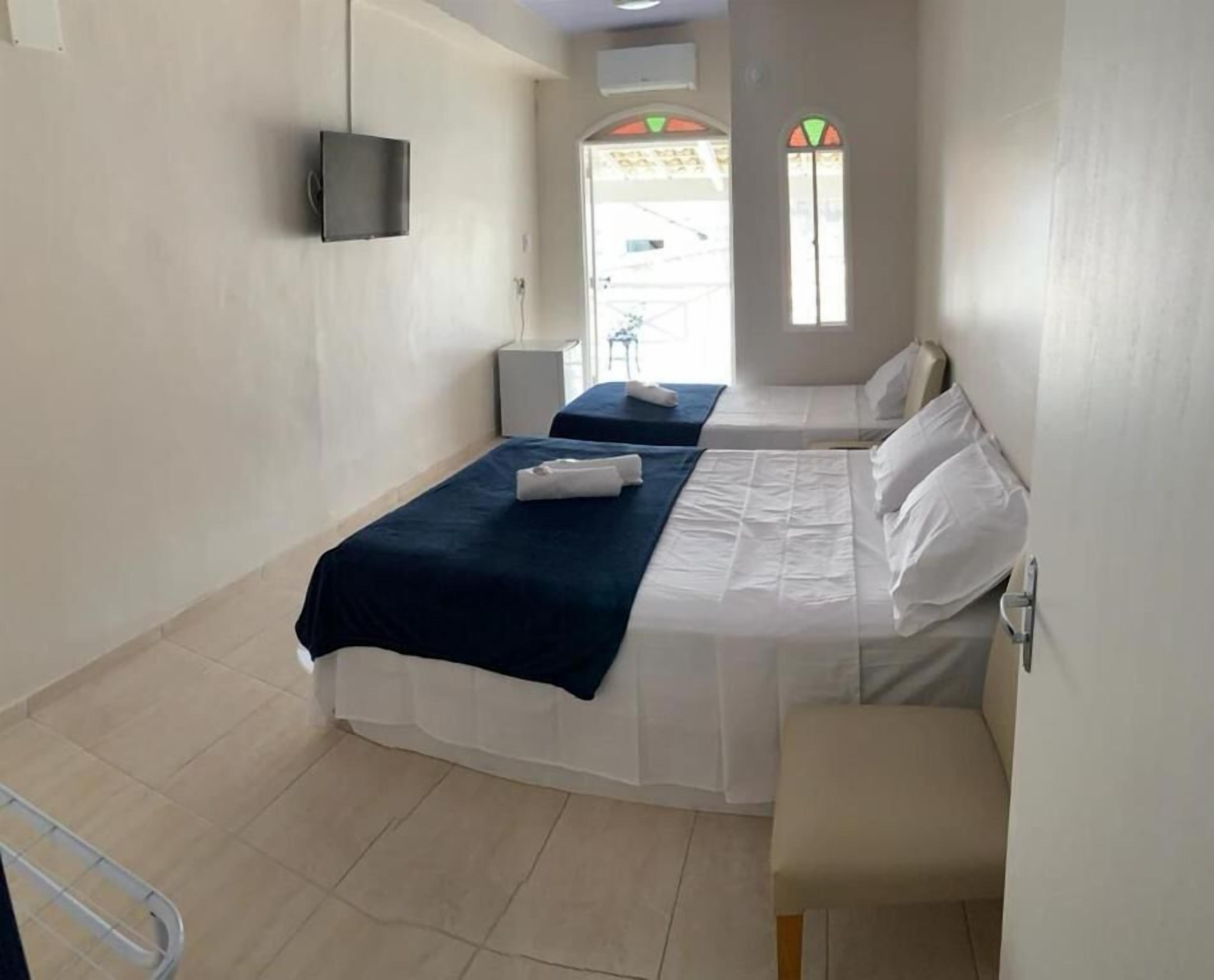Quarto de hotel com duas camas, televisão fixada na parede, uma mesinha e janela com vista para o exterior.