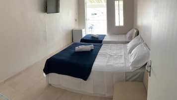 Quarto de hotel com duas camas, televisão fixada na parede, uma mesinha e janela com vista para o exterior.