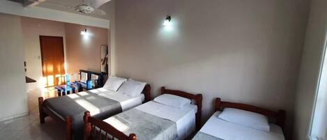A hotel room with three single beds, a ceiling fan, and a small table with chairs.