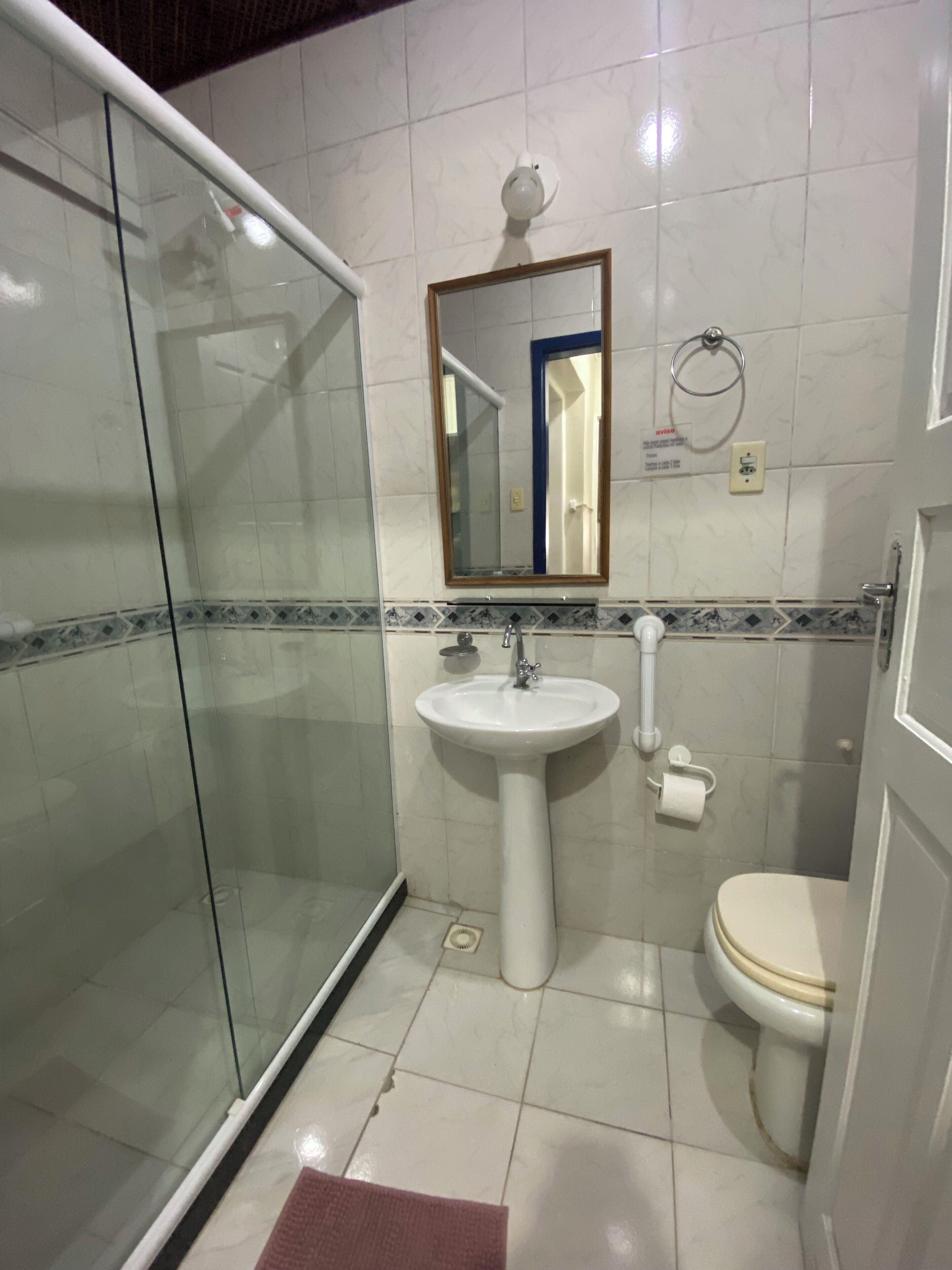 A bathroom with a glass shower enclosure, a pedestal sink, a toilet, and a mirror with a blue frame.