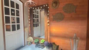 Una habitación con una puerta blanca, un espejo con luces, una pared de ladrillo y un techo con vigas de madera.