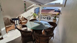 Un balcón con mobiliario de mimbre, una mesa de vidrio y plantas en macetas.