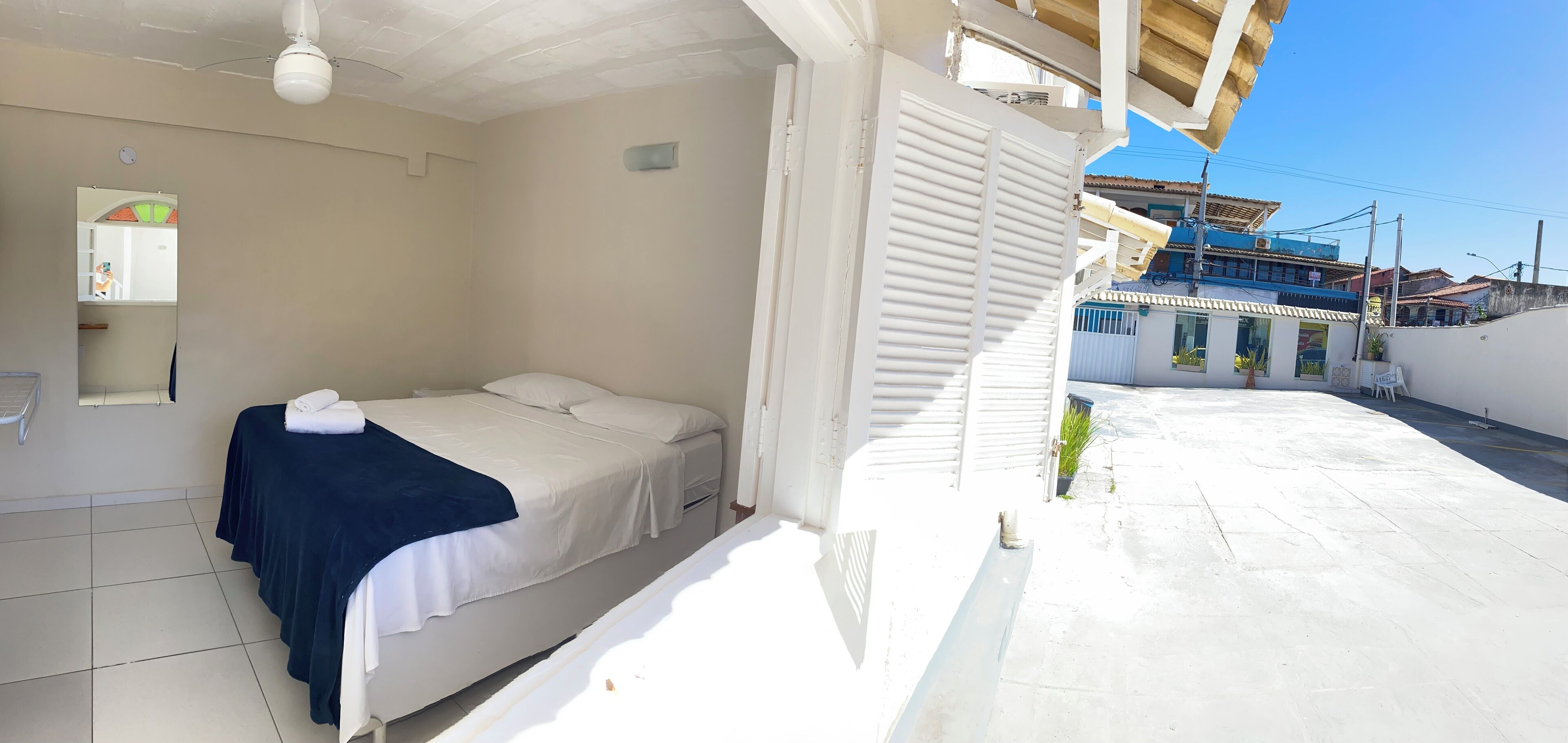 A bedroom with a bed, a ceiling fan, and a view of the street outside.