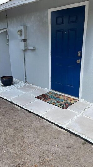 A blue door with a welcome mat, a black bucket, and a utility box on the wall. - Divine Home Beach Retreat (Anavyssos)
