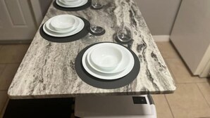 A kitchen with a marble countertop, white plates, black rimmed plates, and wine glasses set for a meal. - Divine Home Beach Retreat (Anavyssos)