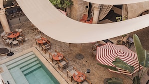 Un patio exterior con varias mesas y sillas, una piscina y un paraguas a rayas.