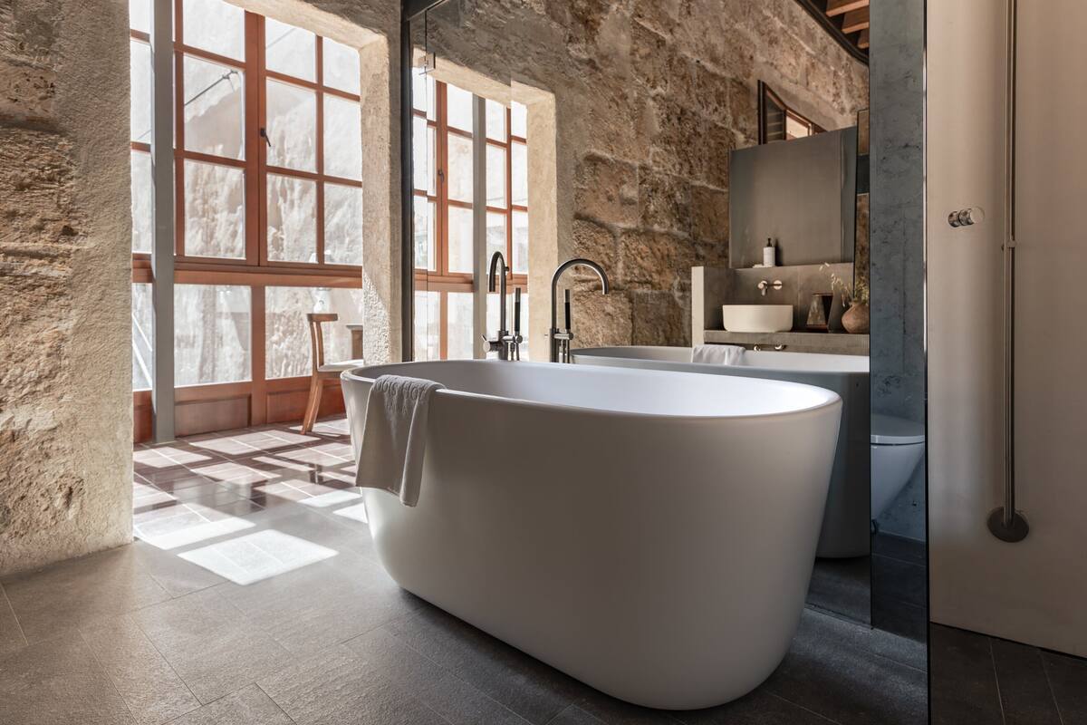 Un baño moderno con una bañera independiente, ventanas amplias y una pared de piedra.
