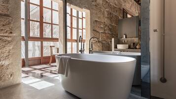 Un baño moderno con una bañera independiente, ventanas amplias y una pared de piedra.