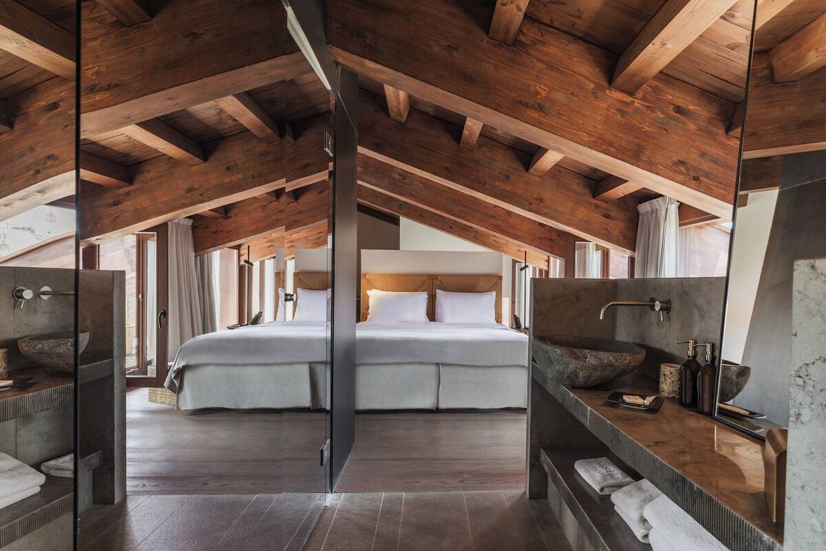 Un dormitorio espacioso con una cama grande, vigas de techo de madera y un baño moderno con un lavamanos y un espejo amplios.