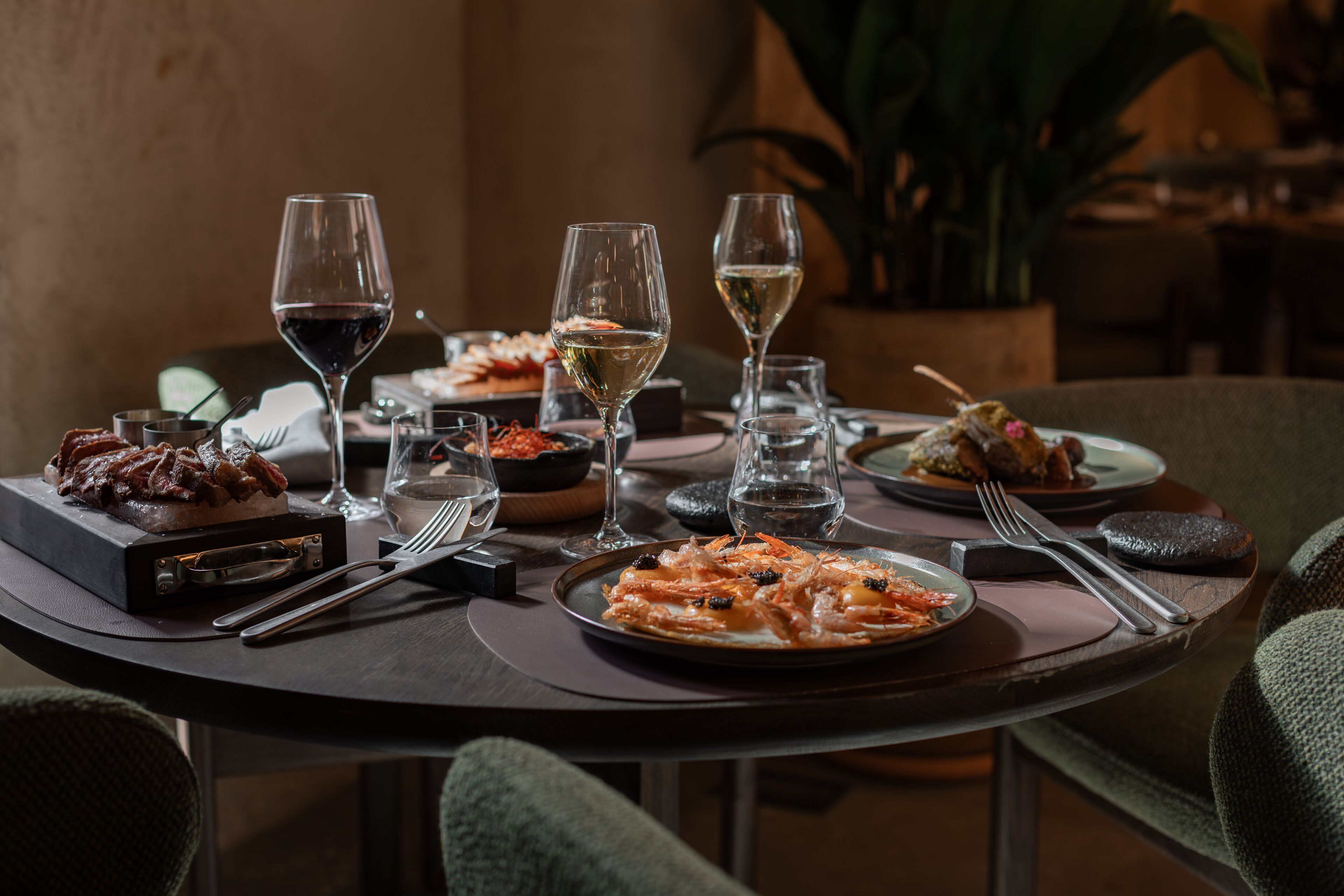 Una mesa de comedor servida con diferentes platos, copas de vino y cubiertos.