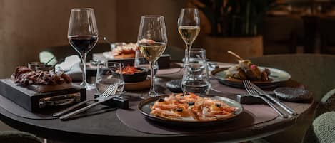 Una mesa de comedor servida con diferentes platos, copas de vino y cubiertos.