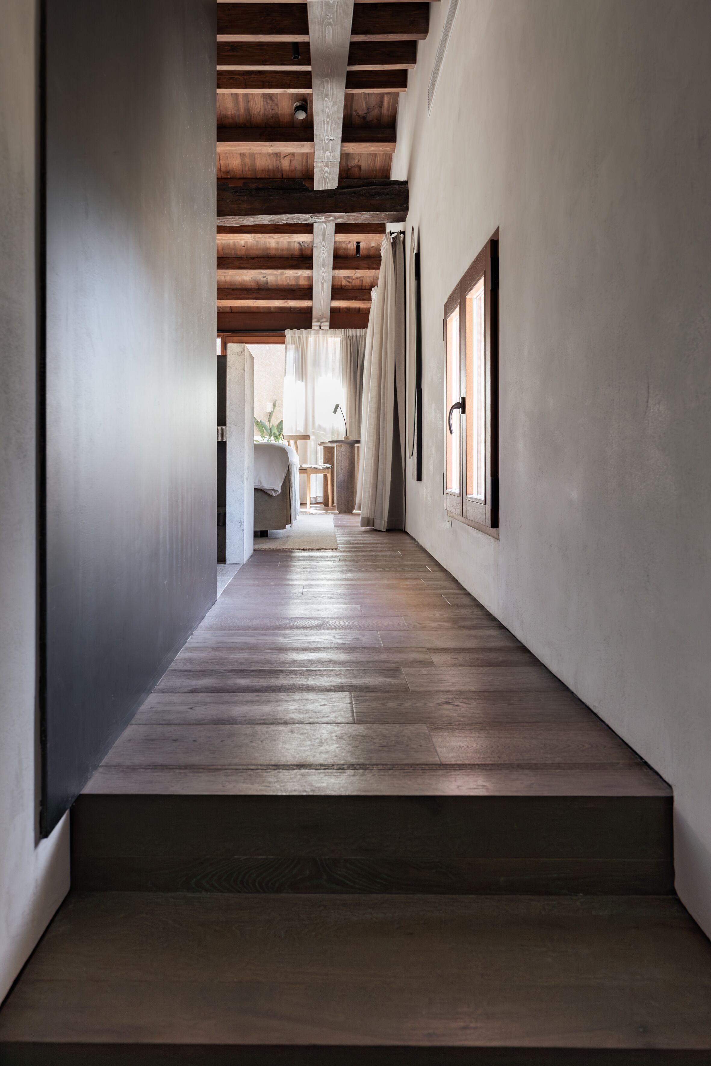 Un couloir avec un plancher en bois, un escalier et un lit à l’arrière-plan.